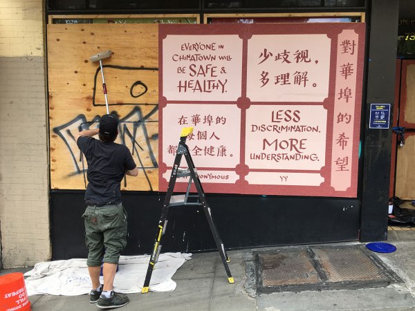 Photo of artwork being installed on graffiti-covered plywood covering storefront windows.